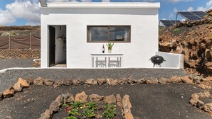 Un edifici petit i blanc amb una finestra, una porta i una taula amb caires a l'exterior.