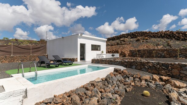 Un edifici modern amb piscina, gandules i una paret de pedra.