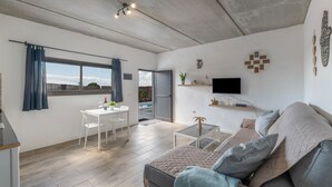Un saló modern amb un sofà, una taula de centre, un televisor fixat a la paret i una zona de menjador amb taula i cadires.
