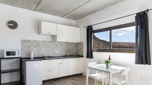 Cuina moderna amb armaris blancs, microones i un rentaplat. Hi ha una taula de menjador amb cadires i una finestra amb cortines.