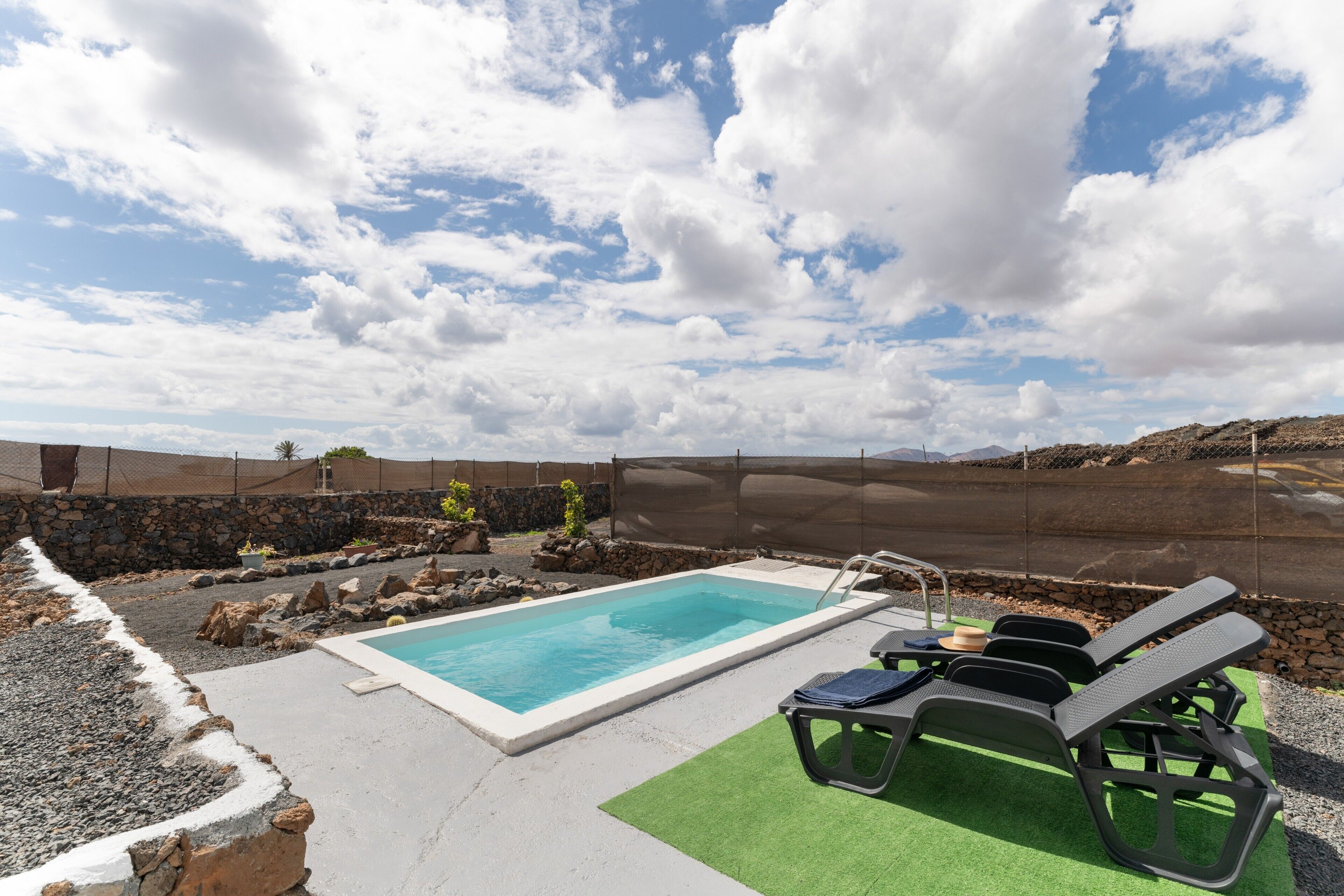A swimming pool with lounge chairs, a stone wall, and a clear sky.