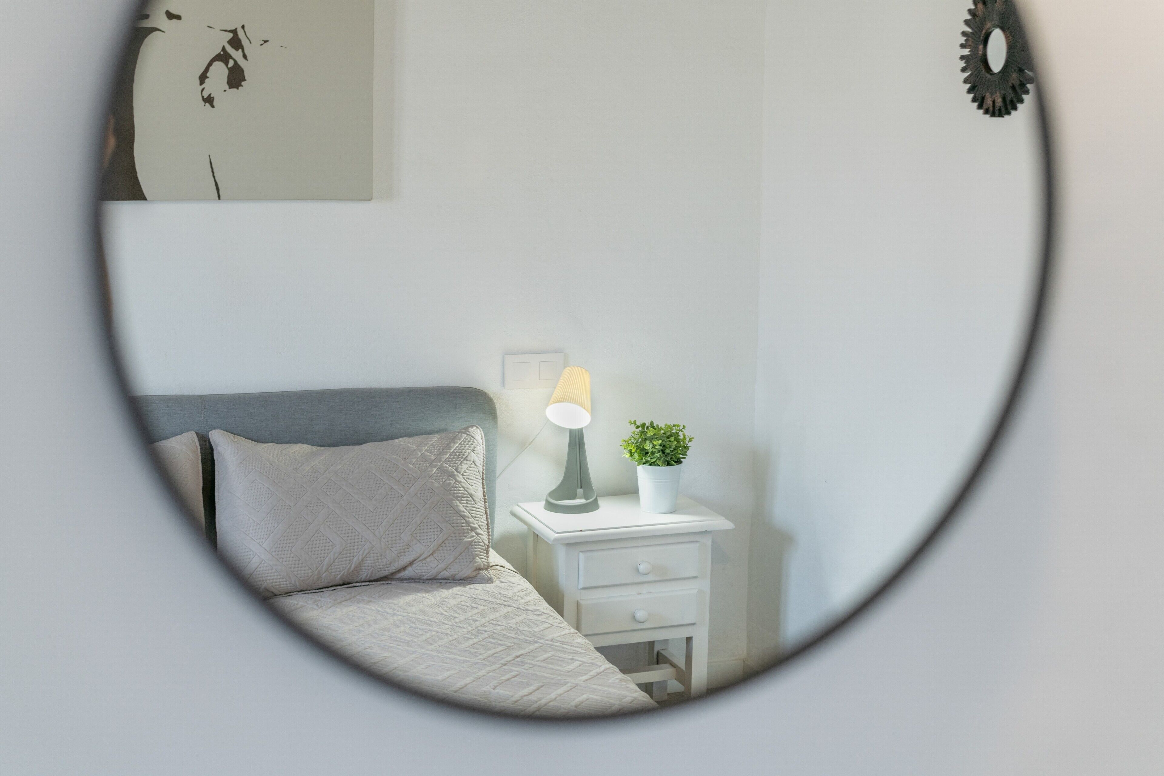 Quarto com cama, mesa de cabeceira com abajur e uma pequena planta em vaso.