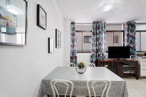 Un'area pranzo con tavolo, sedie, televisione e finestra con tende.