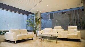A modern living room with a sofa set, a glass coffee table, and large windows with a view of palm trees. - Sun Shine Hotel (Bengaluru)