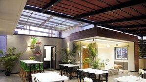 An indoor dining area with tables and chairs, potted plants, and a dog visible through a glass door. - Sun Shine Hotel (Bengaluru)