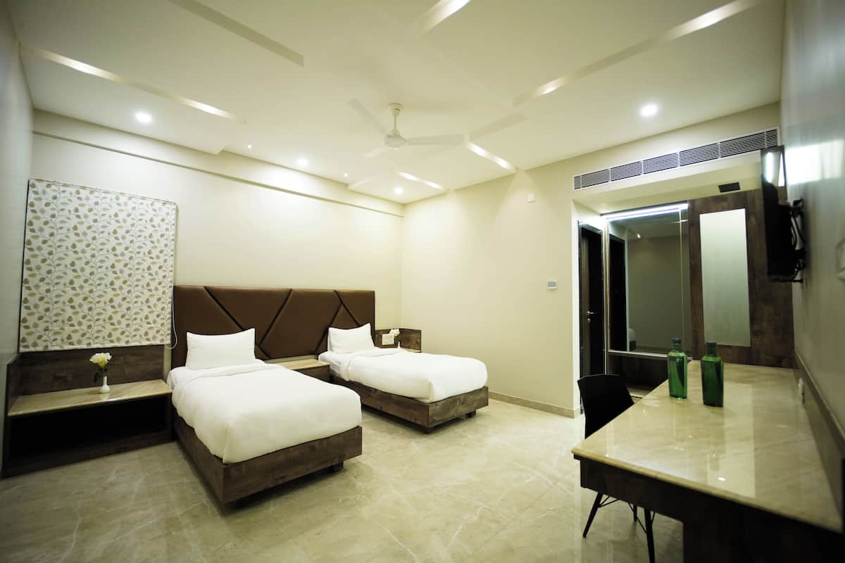A hotel room with two beds, a desk, a mirror, and a ceiling fan.
