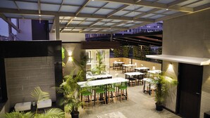An outdoor dining area with multiple tables and chairs, surrounded by potted plants and a modern architectural design. - Sun Shine Hotel (Bengaluru)