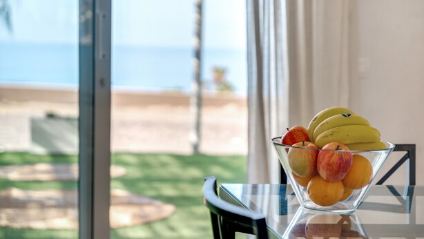 A clear glass bowl with fruits on a table, a view of the beach through a window, and a chair. - Holiday Home 'La Casa del Caballo' with Sea Views, Private Pool and Wi-Fi (Adeje)