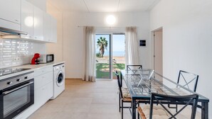 A modern kitchen with a washing machine, a dining area with a glass table, and a view of the beach. - Holiday Home 'La Casa del Caballo' with Sea Views, Private Pool and Wi-Fi (Adeje)