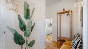Een kamer met een houten vloer, een witte muur met een bladpatroon, een houten bank en een hangende lamp.