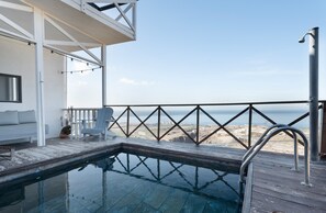 Un espace piscine avec vue sur la plage, une terrasse avec une rambarde et un bâtiment blanc doté d’une fenêtre.
