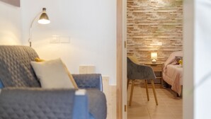 Een kamer met een bank, een stoel, een nachtkastje met lamp en een bed met een roze deken.