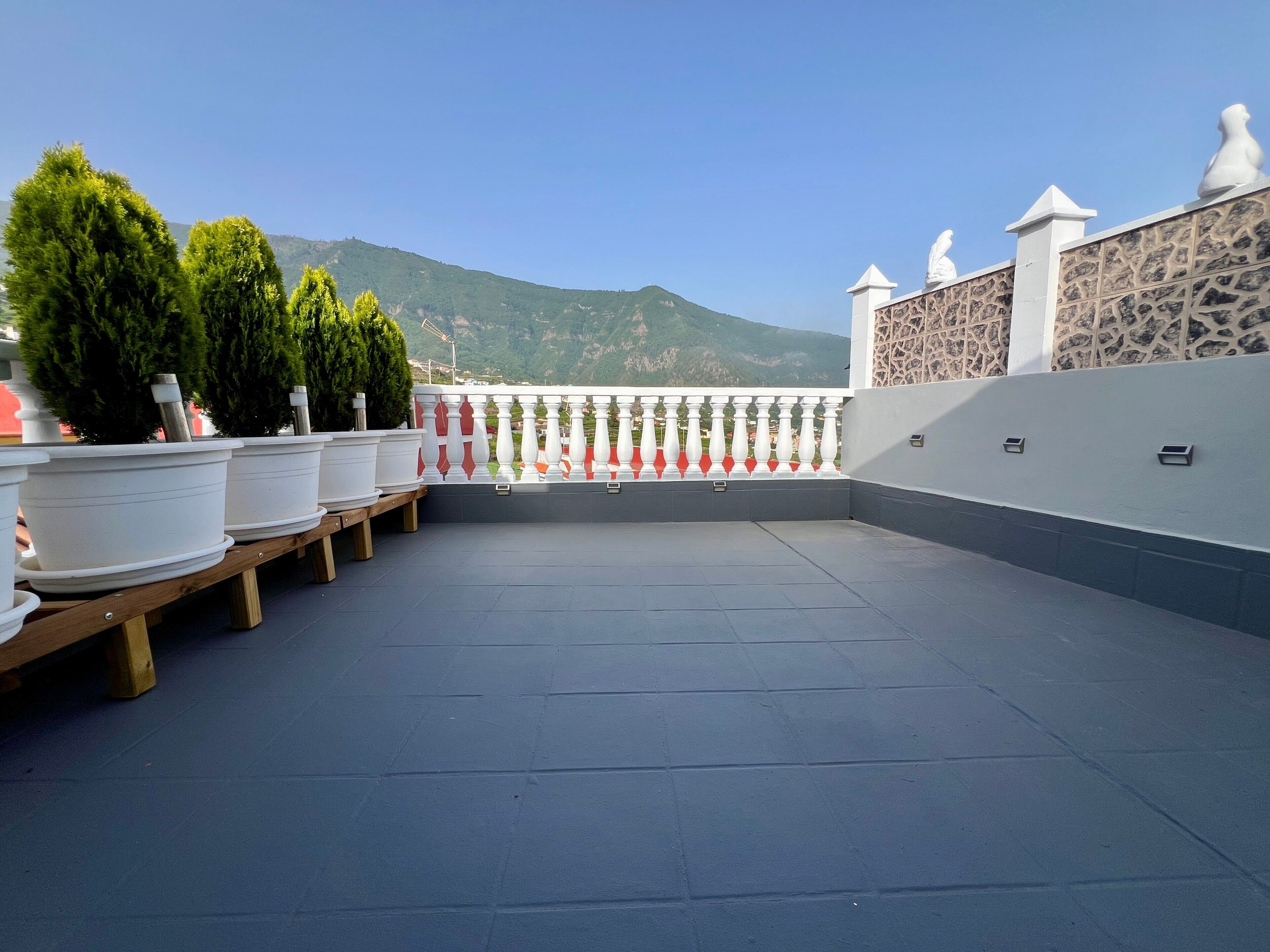 En tagterrasse med plantekasser, gelænder og et bjerglandskab i baggrunden.