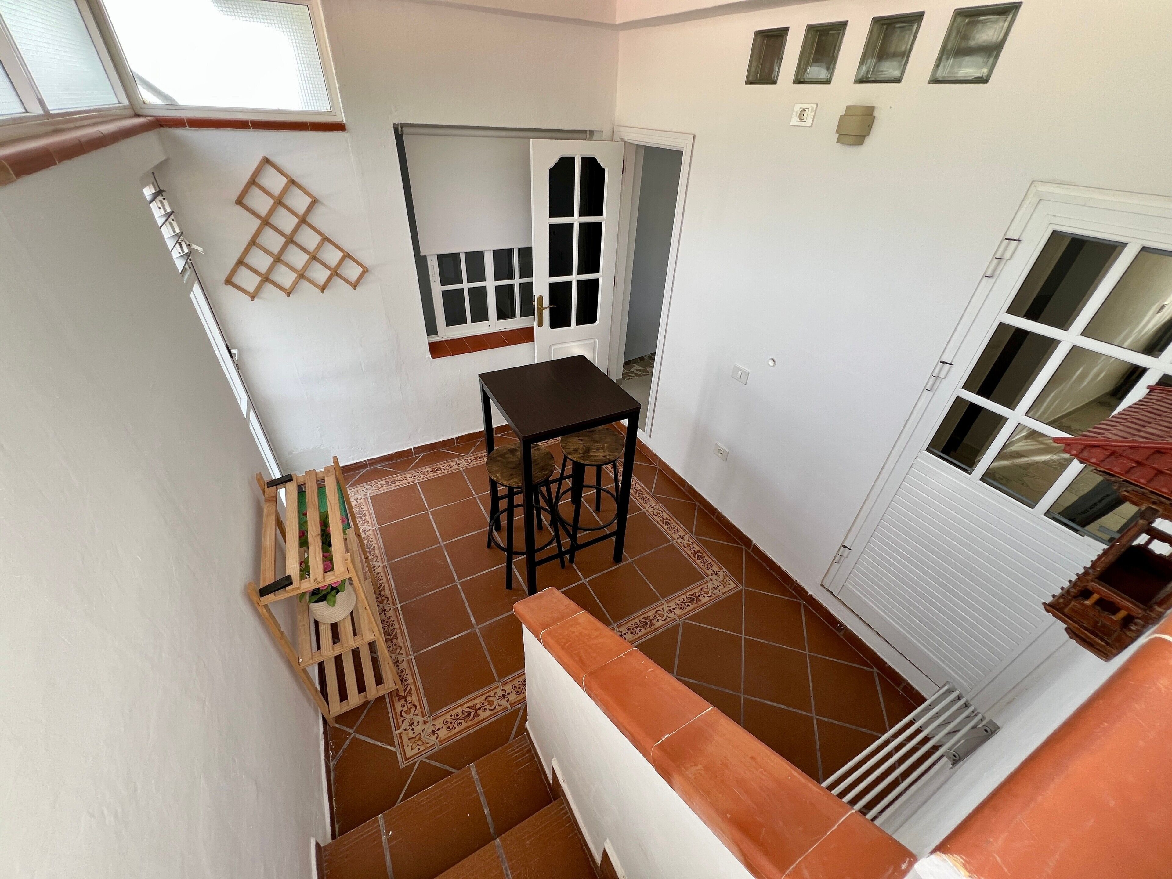 Un pequeño patio amurallado con una mesa y sillas, un banco de madera con una planta y piso de baldosas.