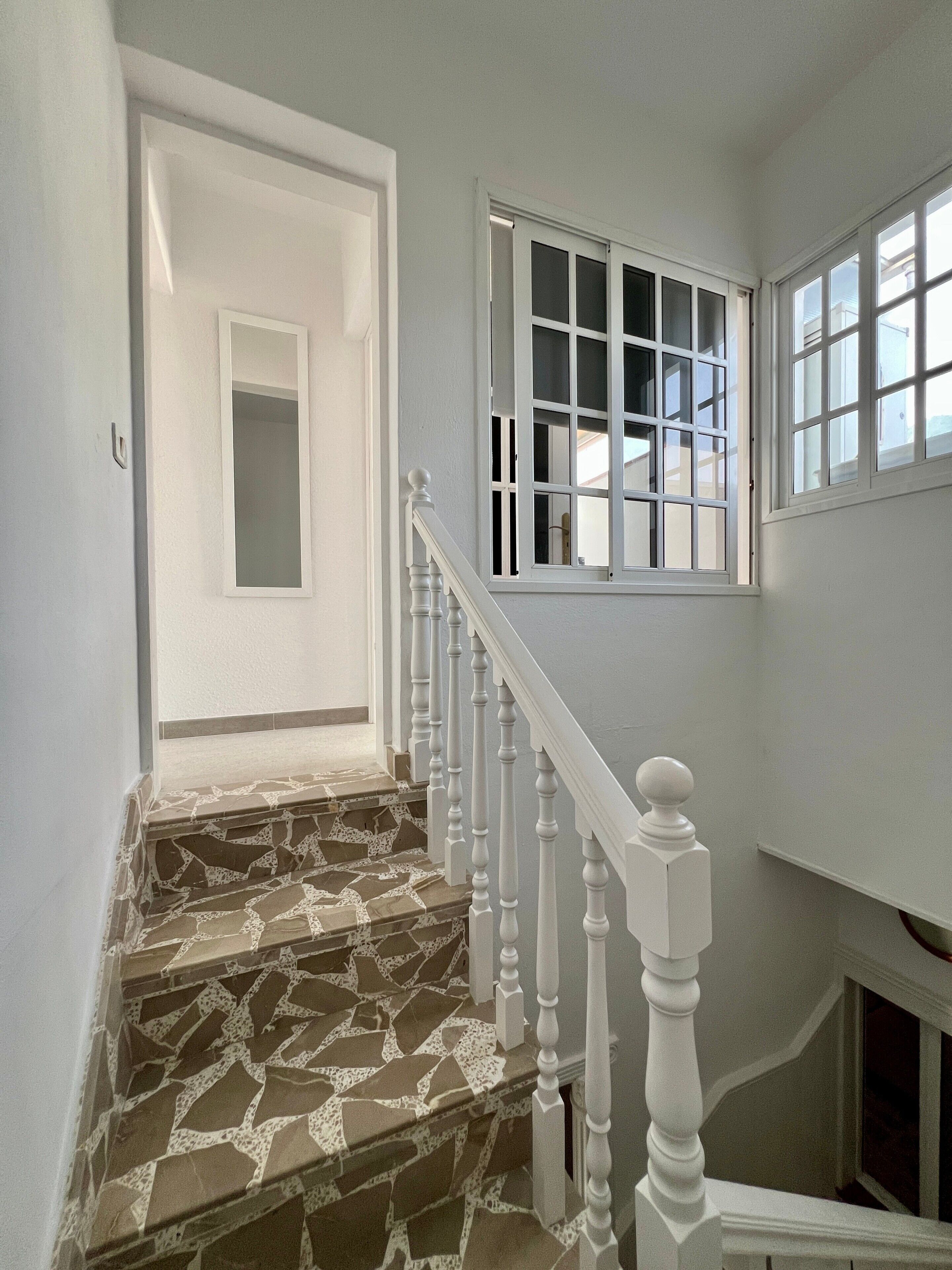 Una escalera con piso de diseño de piedra, balaustres blancos y una puerta al final.