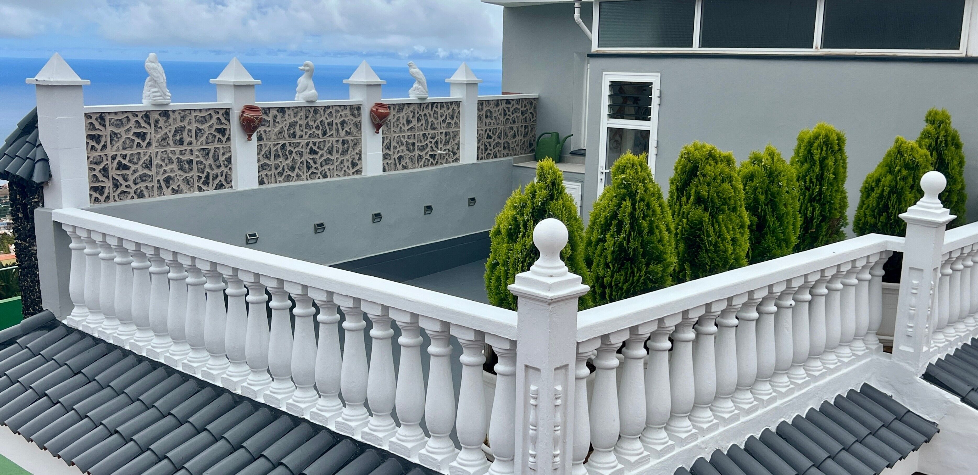 Een balkon met een witte balustrade, een stenen muur met decoratieve details en uitzicht op zee.