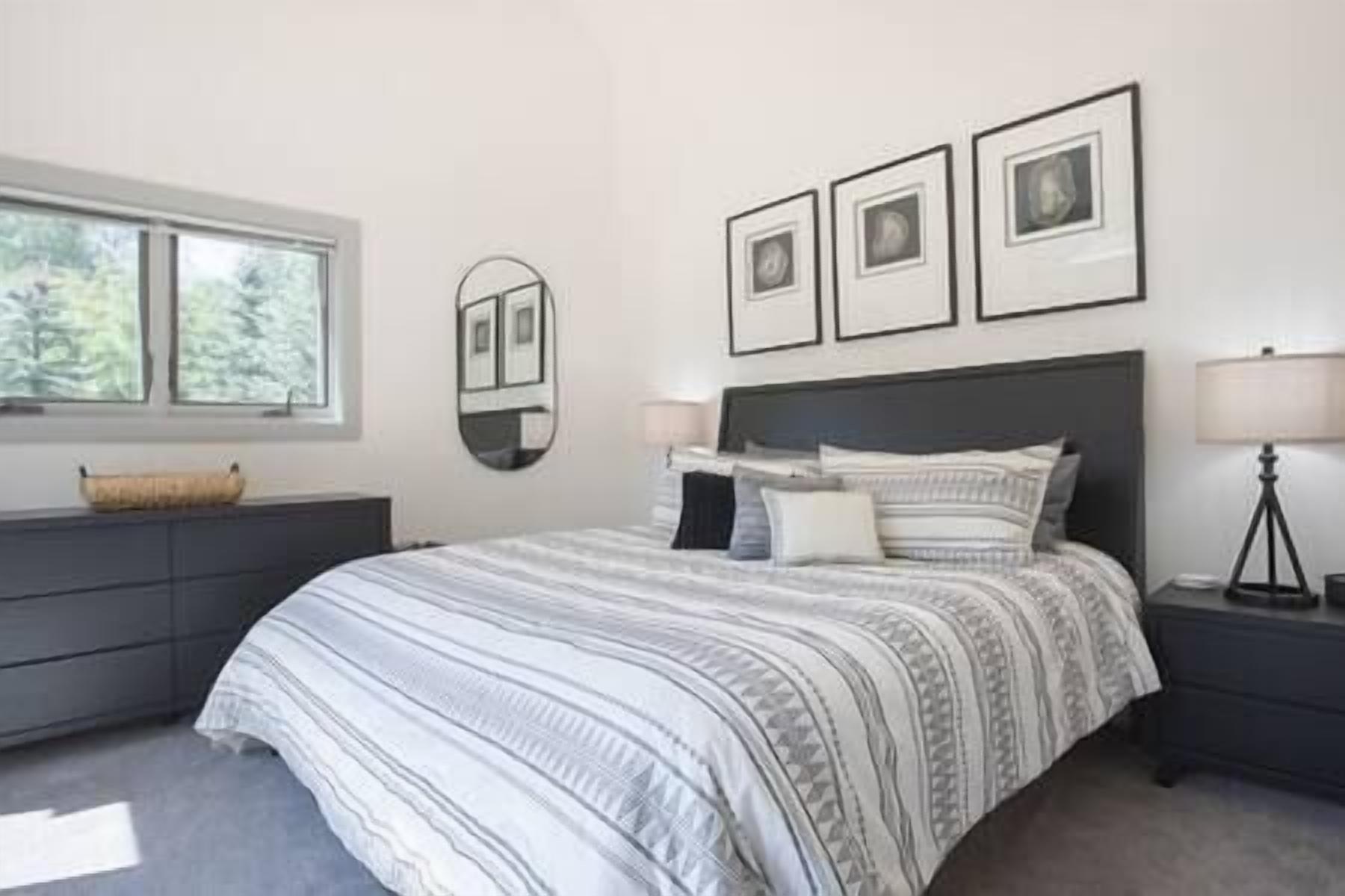 A bedroom with a large bed, a dresser, a mirror, and framed pictures on the wall.
