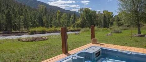 Ein Whirlpool auf einer Holzterrasse mit Blick auf einen Fluss und bewaldete Berge.
