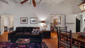 Uma sala de estar ampla com um sofá marrom escuro, um tapete estampado, uma mesa de centro de madeira e uma área de jantar com mesa e cadeiras de madeira.