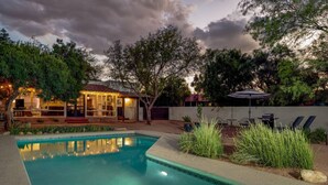 A swimming pool with a tiled edge, surrounded by a patio area with outdoor furniture and a covered seating area.