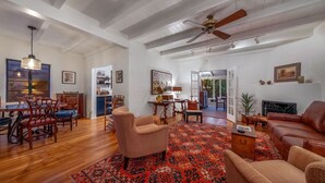 A spacious living room with a large red patterned rug, a brown leather sofa, a wooden coffee table, and a ceiling fan.