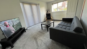 Una sala de estar con televisor, sofá, mesa de centro y una silla.