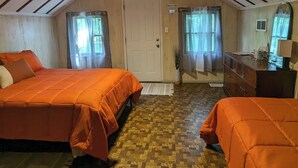 Une chambre avec deux lits, un ventilateur de plafond, une porte et une fenêtre avec des rideaux.