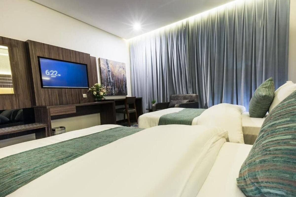 Habitación de hotel con dos camas, televisión, escritorio y un ventanal grande con cortinas.