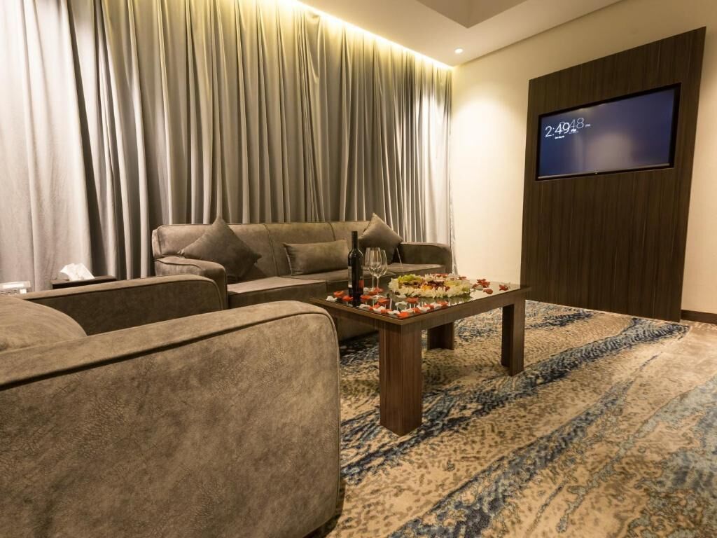 A modern living room with a sofa, a coffee table with snacks, a TV on the wall, and a large window with curtains.