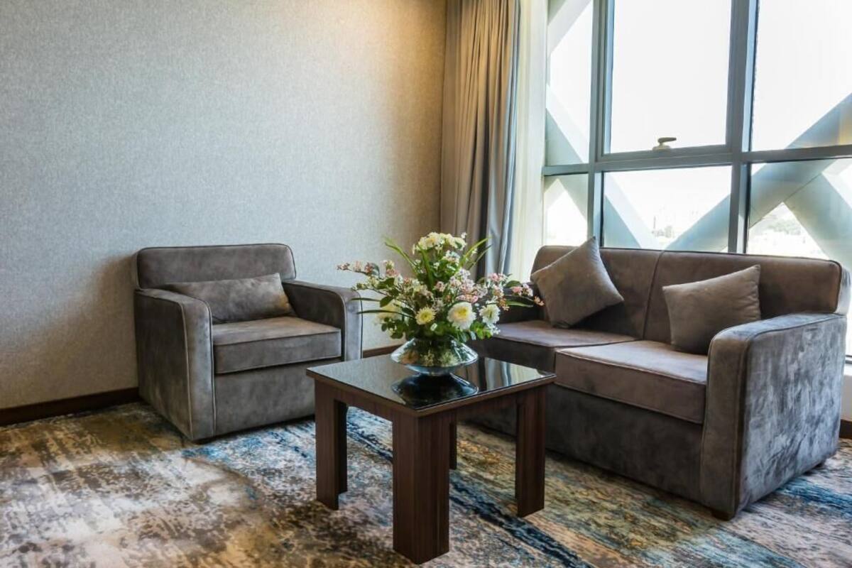 Una habitación con dos sofás, una pequeña mesa con un jarrón de flores y un ventanal con cortinas.