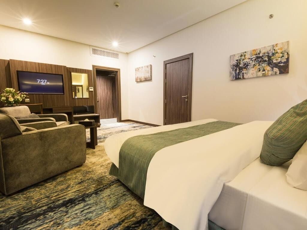 Ein Hotelzimmer mit einem großen Bett, einer Couch, einem Fernseher und einem Gemälde an der Wand.