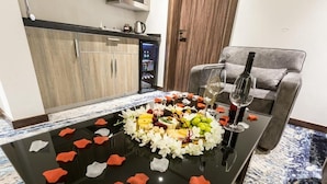 A dining table with a fruit and cheese platter, wine glasses, and decorative flower petals. - White Diamond Hotel Sari (Jeddah)