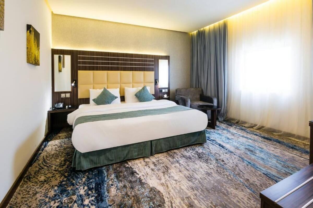Habitación de hotel con una cama grande, un escritorio, una silla y una ventana con cortinas.