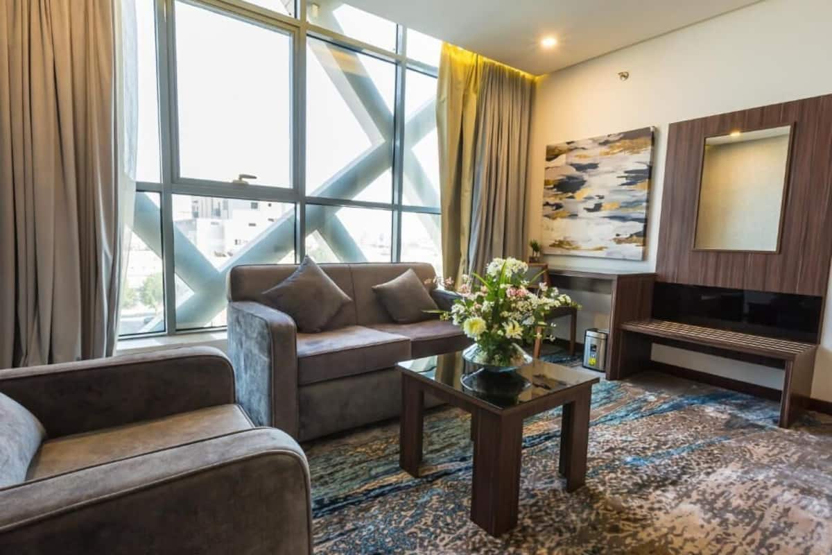 Una sala de estar moderna con un sofá, una mesa de centro con flores, un televisor y un ventanal con cortinas.