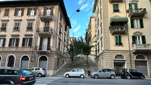 A street view with cars parked on the side, buildings with balconies, and a clear sky.
