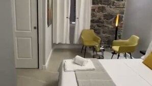 A hotel room with a bed, two yellow chairs, a stone wall, and a painting on the wall.