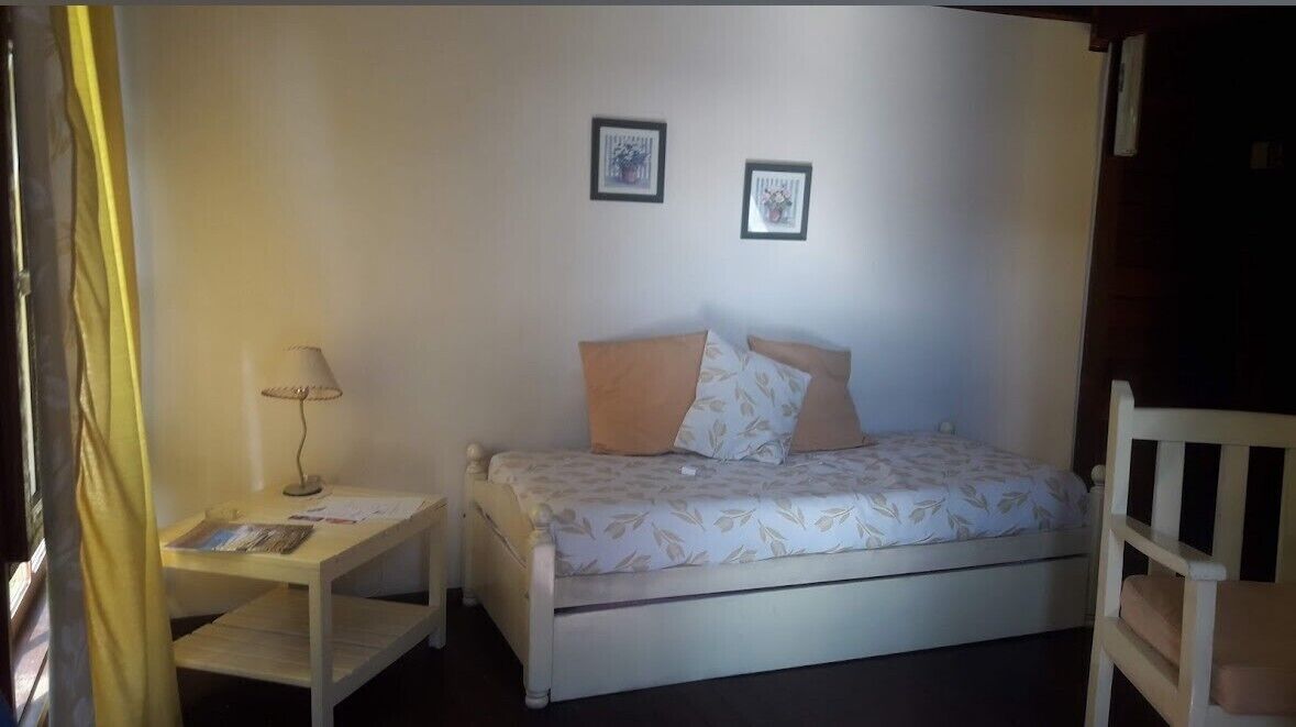 A small, single-bed room with a bedside table, a chair, and two framed pictures on the wall.