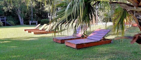 A grassy area with two wooden loungers under a palm tree.