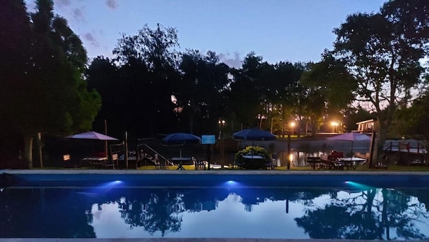 Una piscina con sombrillas y sillas de descanso, rodeada de árboles y un edificio al fondo.