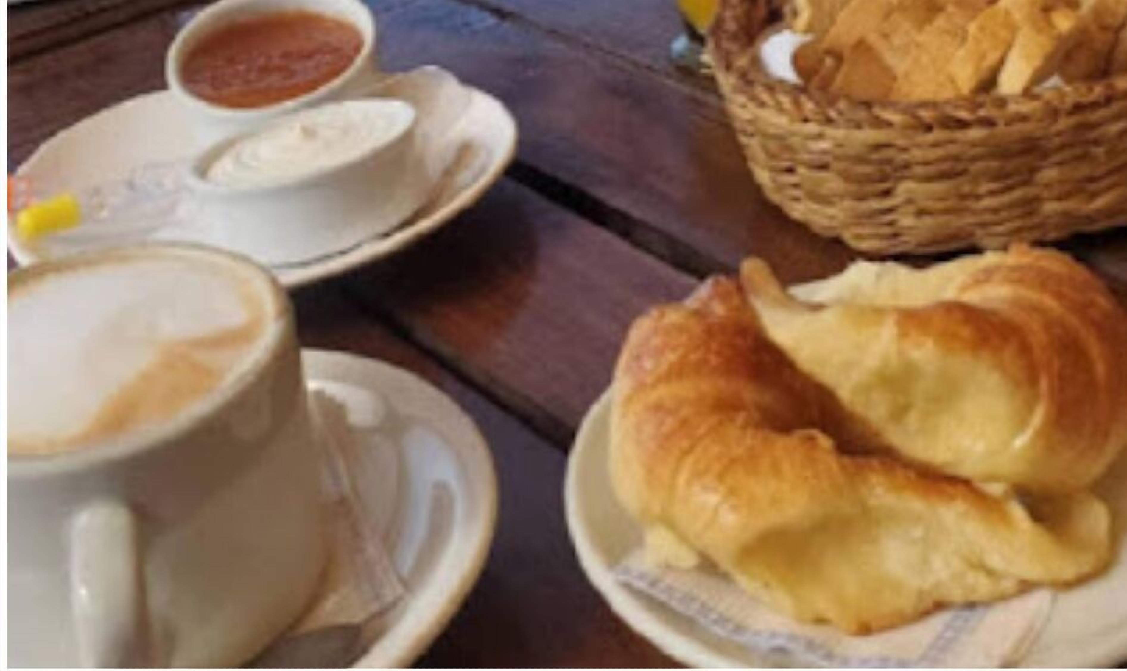 A table with a basket of bread, a cup of coffee, and a bowl of soup.
