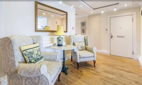 Une pièce comprenant deux fauteuils à motifs, une petite table ronde avec une lampe et un miroir accroché au mur.