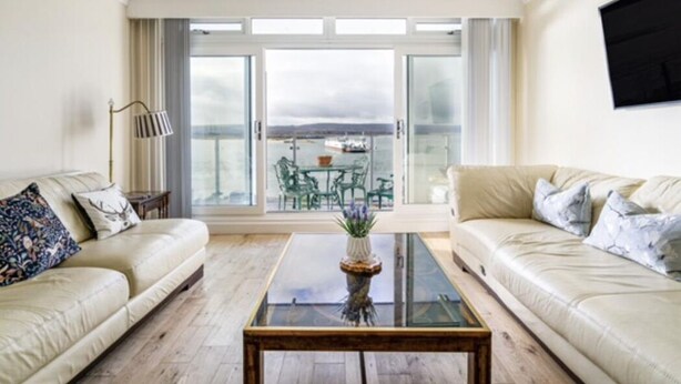 Un salon avec deux canapés, une table basse en verre et une vue sur un balcon aménagé avec du mobilier d’extérieur.