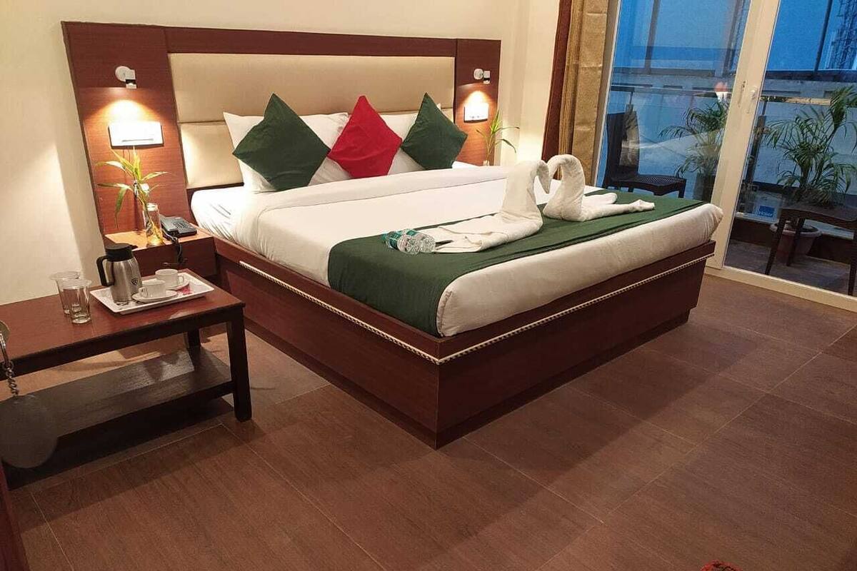 A hotel room with a large bed, bedside tables, a nightstand, and a view of the outside.