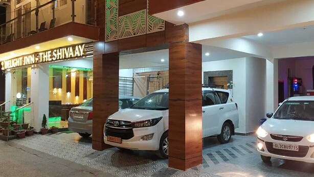 A hotel entrance with a sign reading "The Shivaay." Two cars are parked in front, and the building features a modern design with wooden pillars. - Hotel The Shivaay - Delight Inn  (Rishikesh)