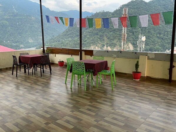 A terrace with a table and chairs, a potted plant, and a view of a mountainous landscape. - Hotel The Shivaay - Delight Inn (Rishikesh)