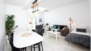 Ein modernes Wohnzimmer mit einem weißen Sofa, einem braunen Sofa, einem Esstisch mit Stühlen und einer großen Kühlpflanze.