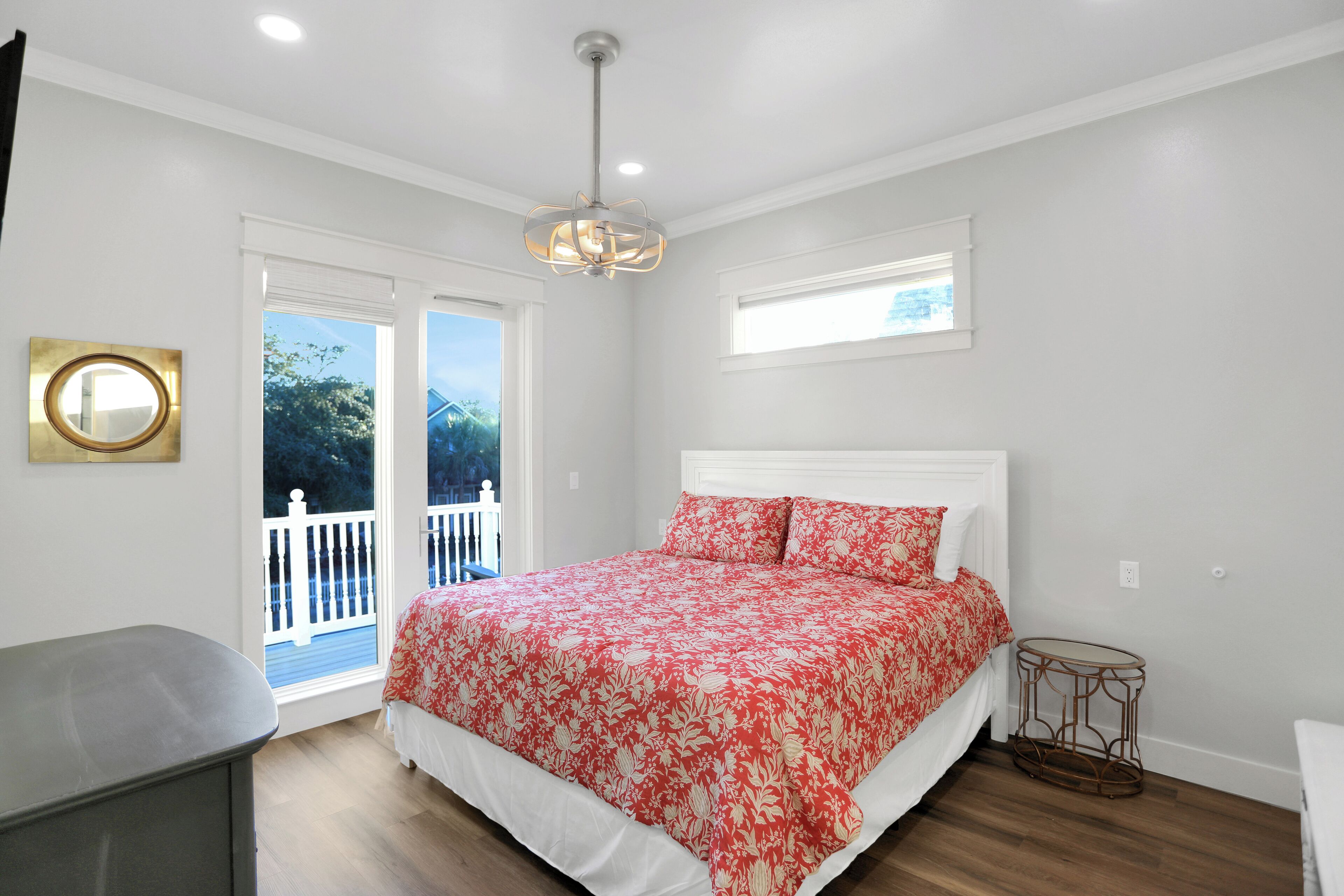 A bedroom with a large bed, a small side table, a ceiling light, and a window with a view of the outdoors.