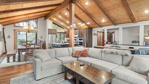 A spacious living room with a large sectional sofa, wooden ceiling beams, and a dining area with a wooden table and chairs. - Edgewater Escape in Dollar Point Tahoe City (Tahoe City)