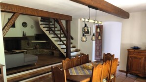 A dining area with a wooden table and chairs, a staircase leading to a loft, and a kitchen in the background.