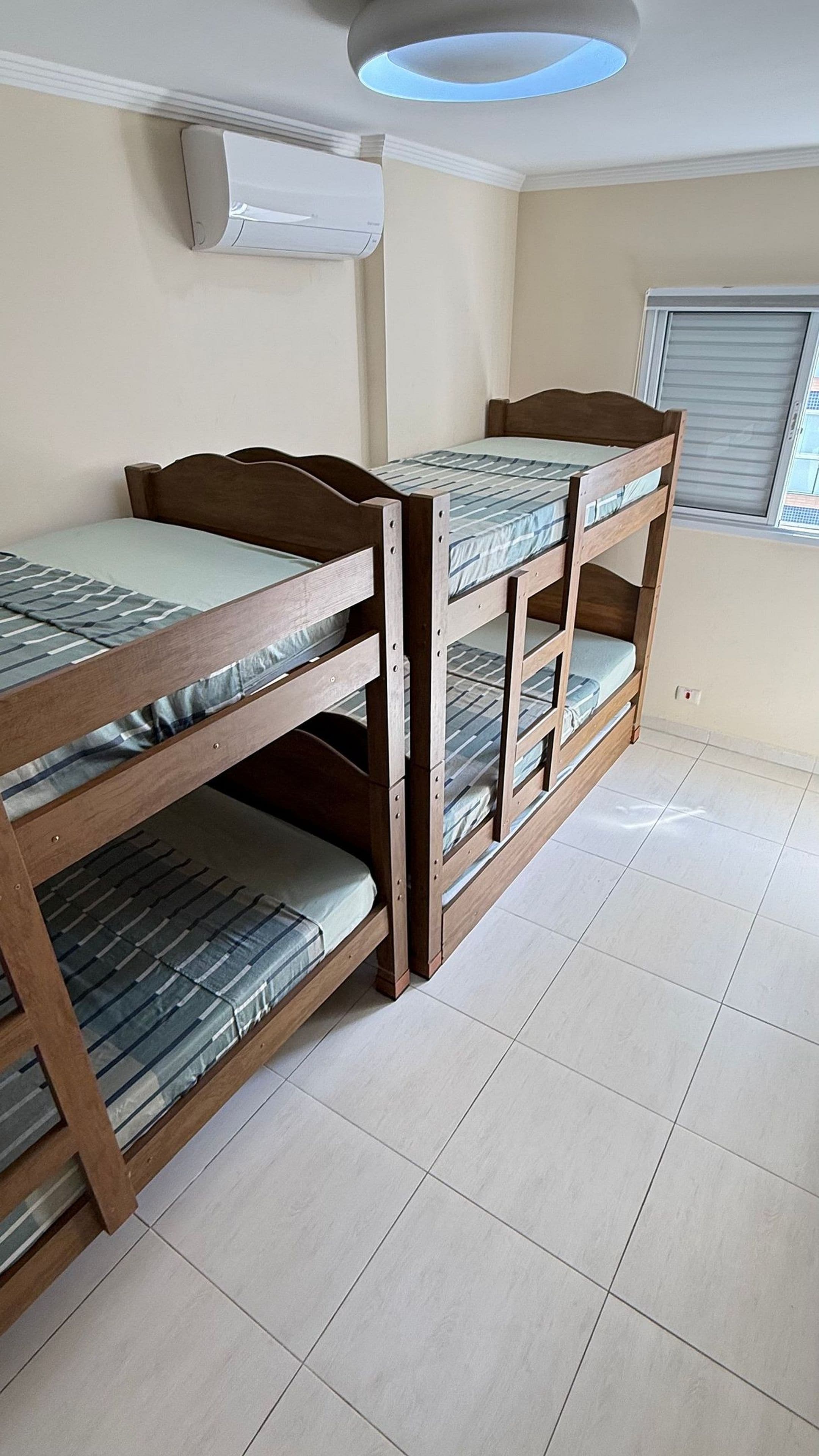Quarto com beliches, ventoinha no teto e janela com cortinas.